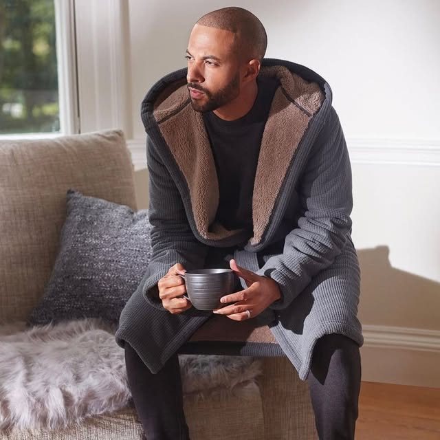Man seated on a sofa wearing a hooded grey waffle dressing gown